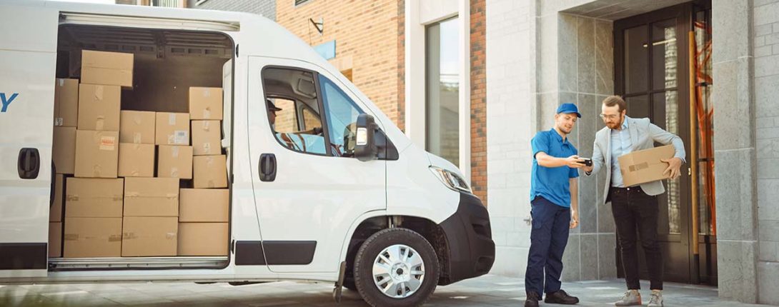 white delivery van with side door open containing packages. men meeting at front of van receiving package